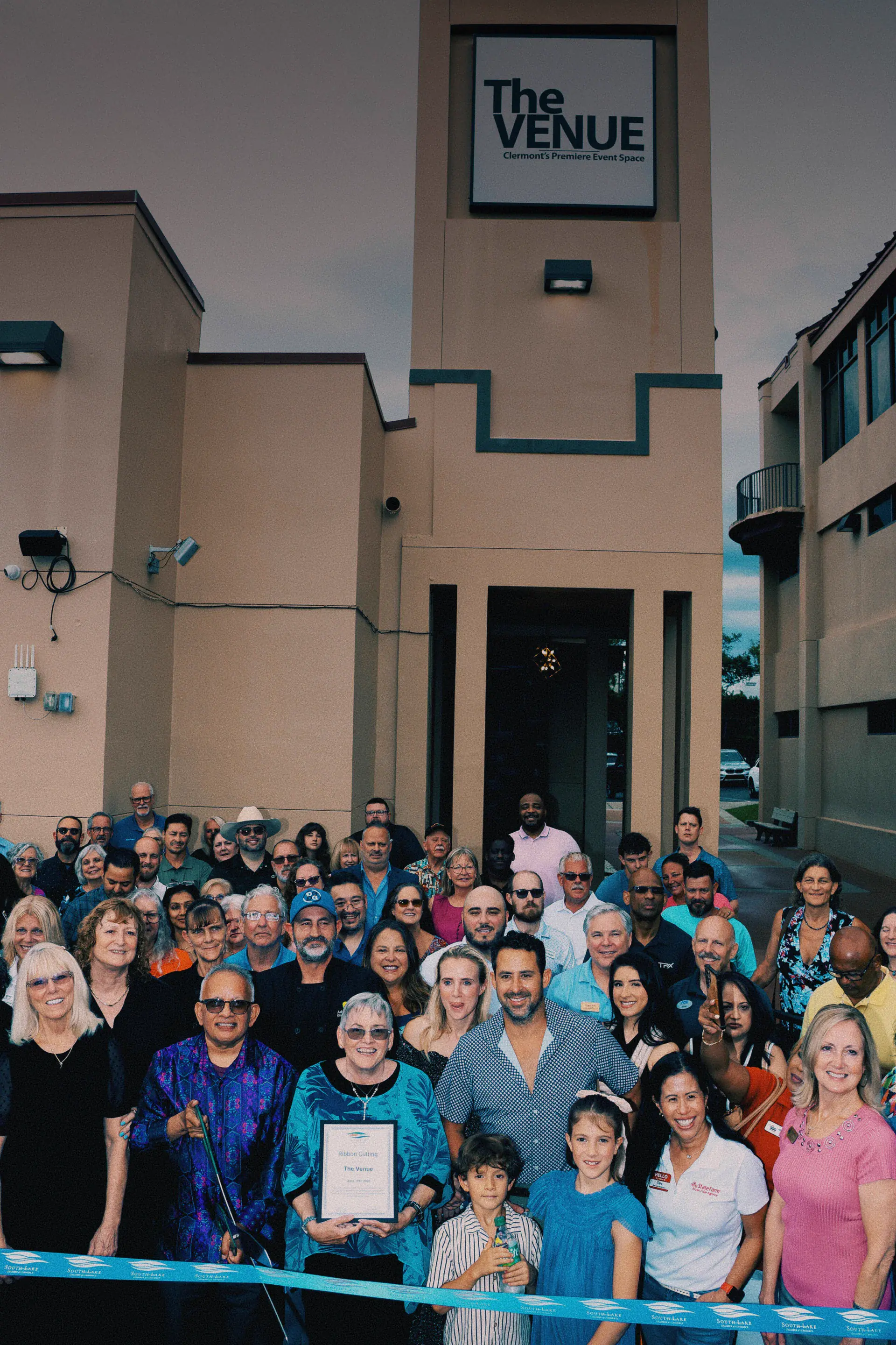 Group photo celebrating the grand opening ribbon cutting in front of The Venue Clermont building entrance with prominent venue signage